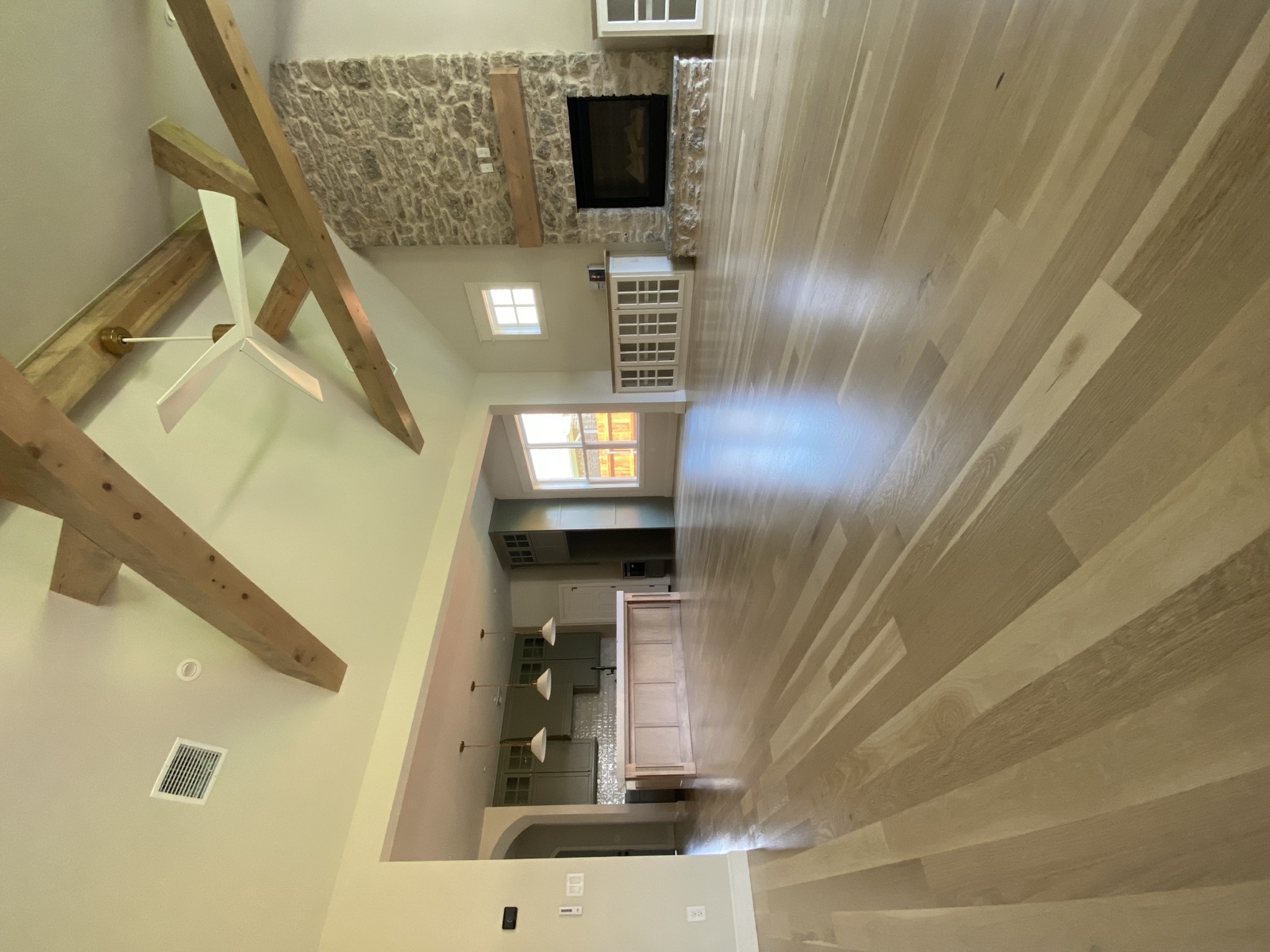 Wide-plank white oak floor in a great room with timber beams and stone fireplace
